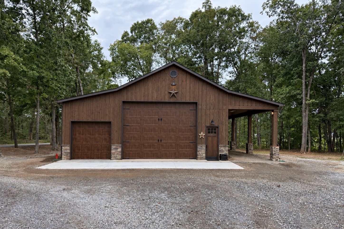 Completed stained board and batten detached workshop garage with oversized bays and covered side porch