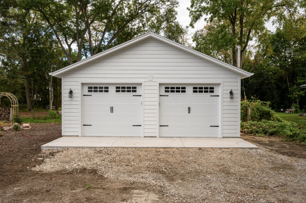 Completed white two-bay detached garage with horizontal siding and carriage-style doors