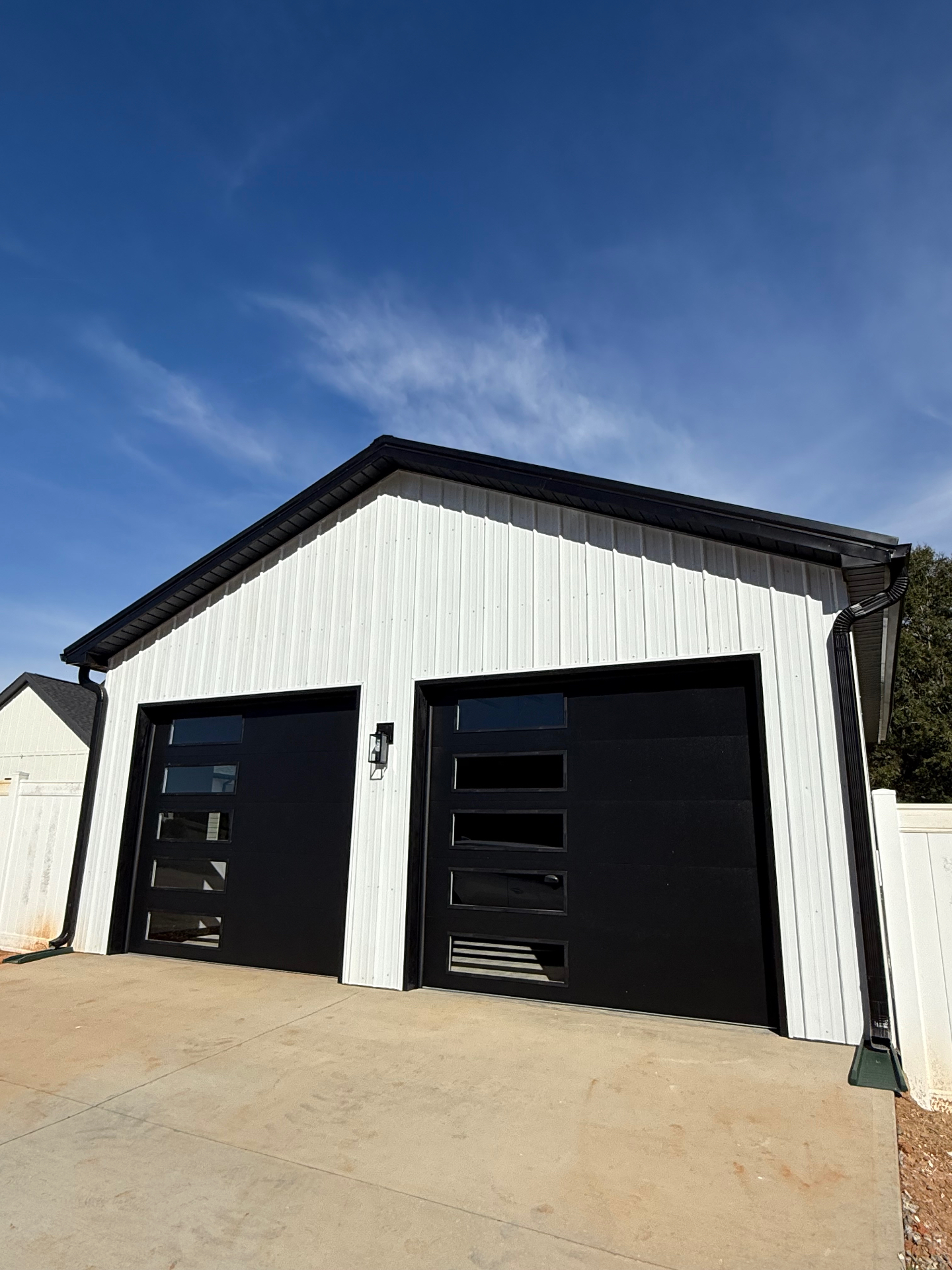Modern detached garage with black contemporary doors and white metal siding